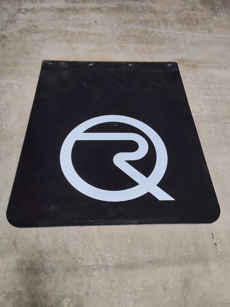 Black rubber mud flap with white Q-shaped logo on concrete surface